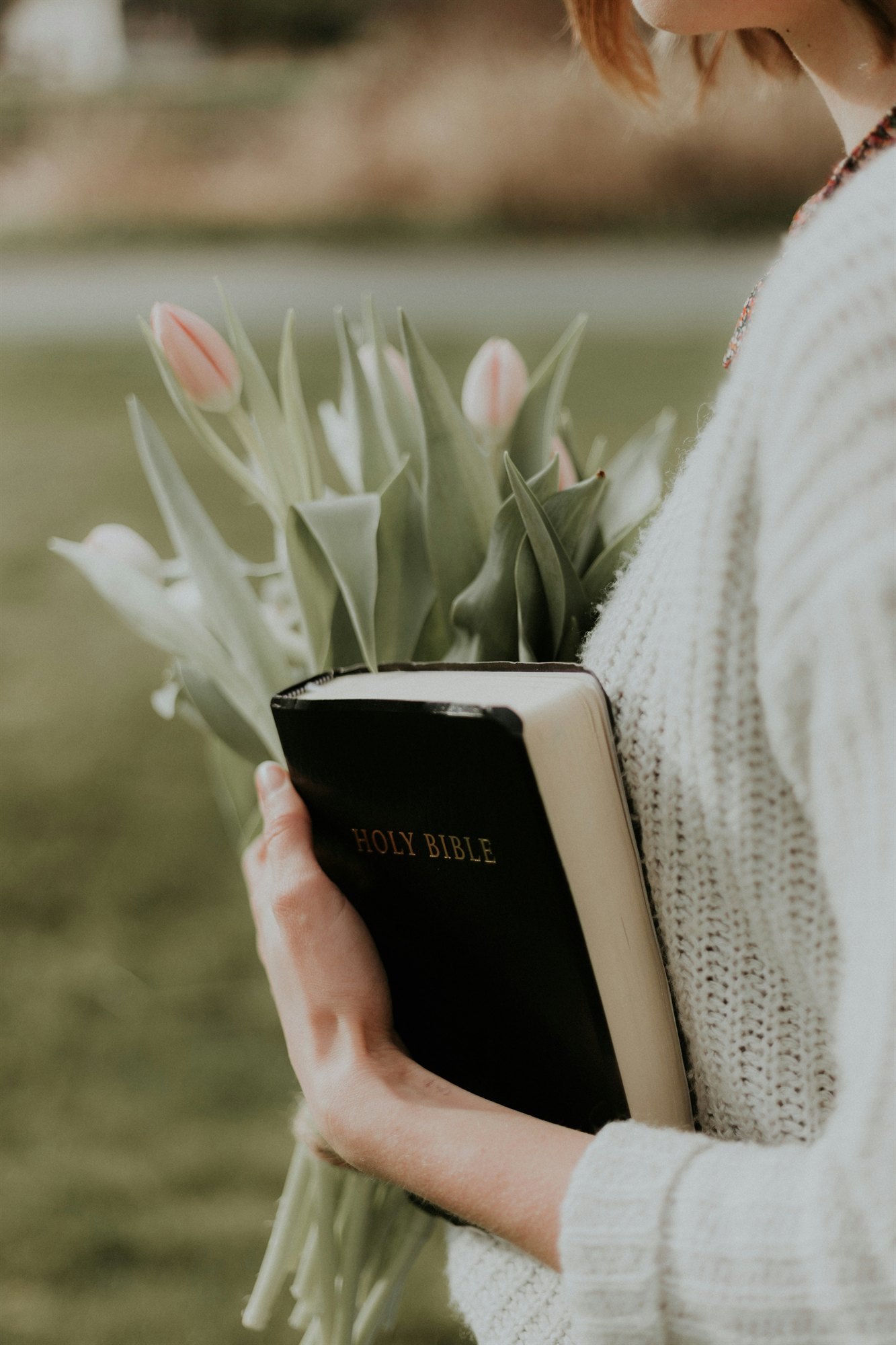 A woman holding a Bible in a quiet moment among flowers